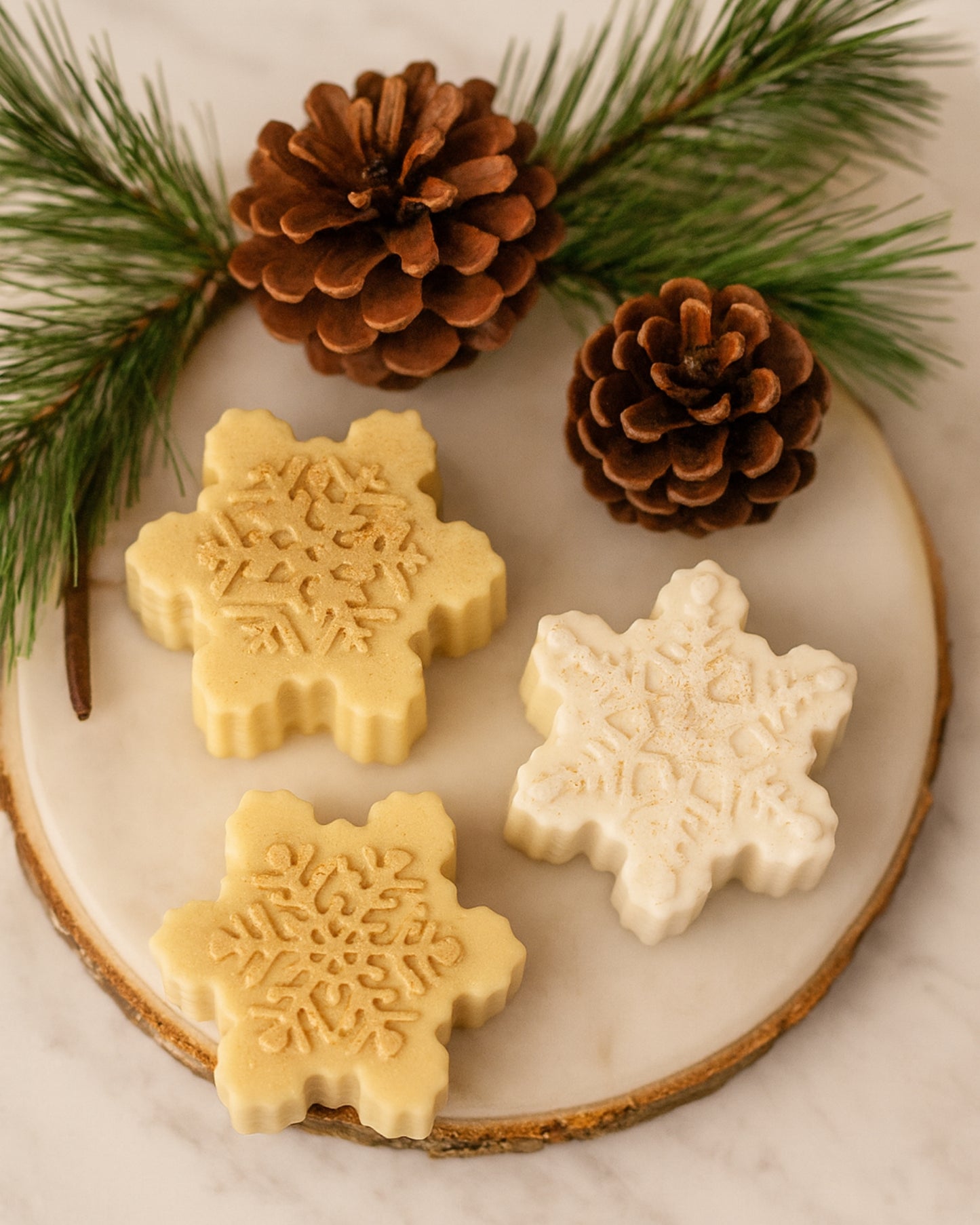 Set of DEOS Co. Arctic Snowflake handmade soaps on a marble tray with pinecones — crafted in Greece from botanical oils and natural ingredients for a clean, festive skincare ritual.