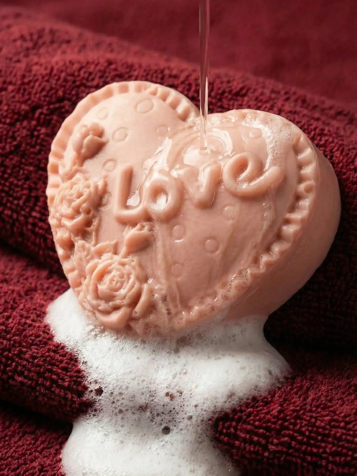 Heart-shaped soap with 'LOVE' and floral designs on a red towel by DEOS CO. Valentine Collection. Rose geranium and vanilla soap by DEOS CO
