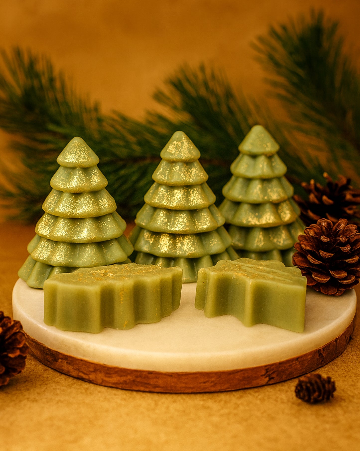 Three handcrafted green Christmas tree soaps from DEOS Co.’s Olympian Pine Collection, enriched with botanical oils, pine and orange scent, and gold shimmer for a luxurious festive display.