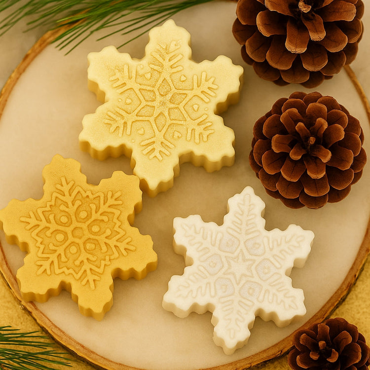 Three handcrafted snowflake soaps from DEOS Co.’s Christmas Collection rest on a marble and wooden tray, surrounded by pinecones and pine branches. Warm golden lighting creates a luxurious, festive, and natural Christmas atmosphere.