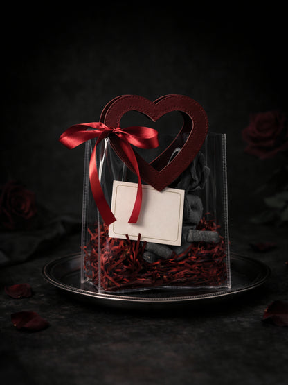 Transparent DEOS CO Valentine's Day gift bag with wine red heart-shaped handle and soaps inside, styled on a plate against a dark background