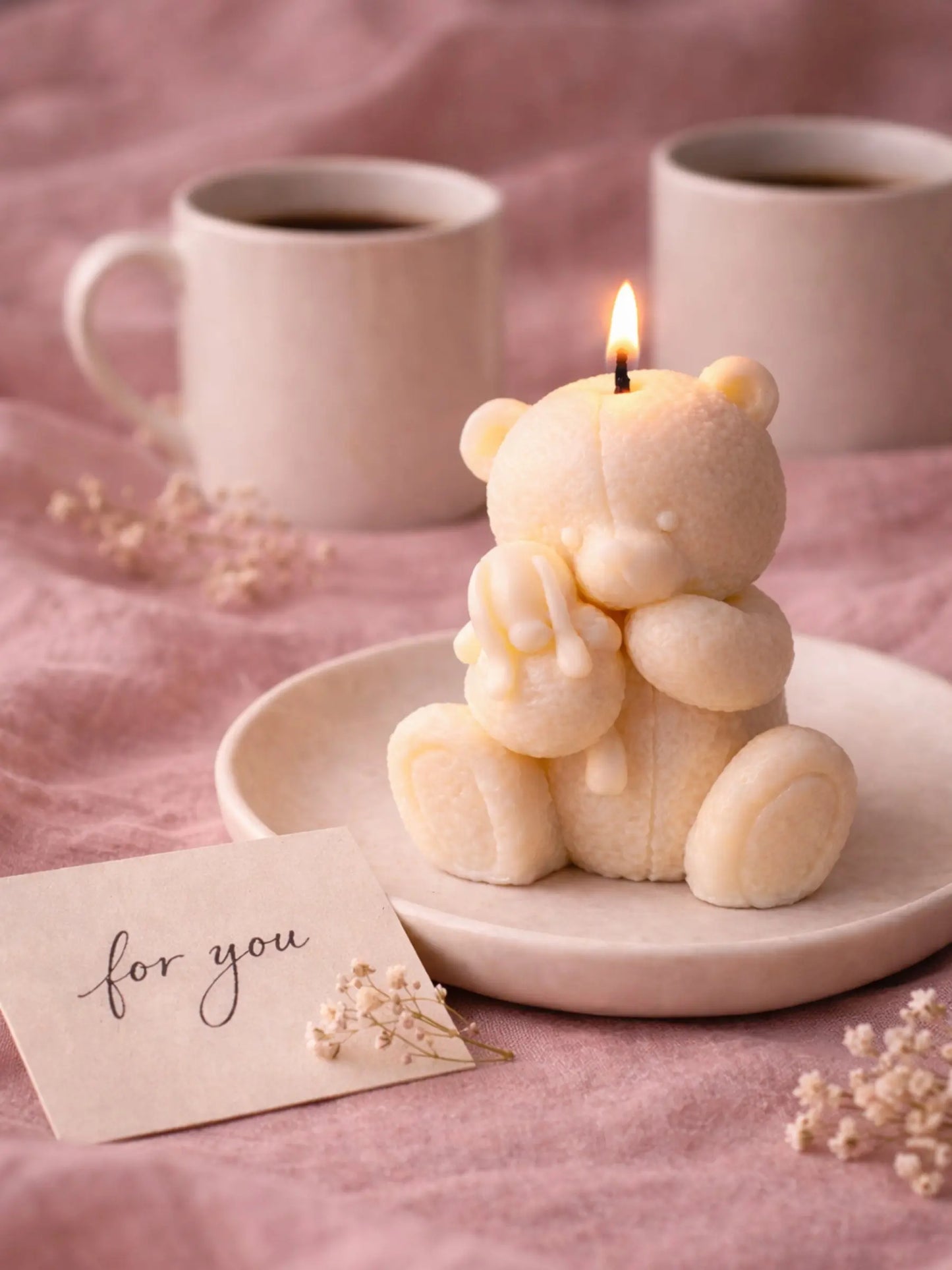 Romantic Valentine’s Day scene with lit teddy bear soy candle, coffee mugs and handwritten gift note by DEOS CO, Elior SOY CANDLE
