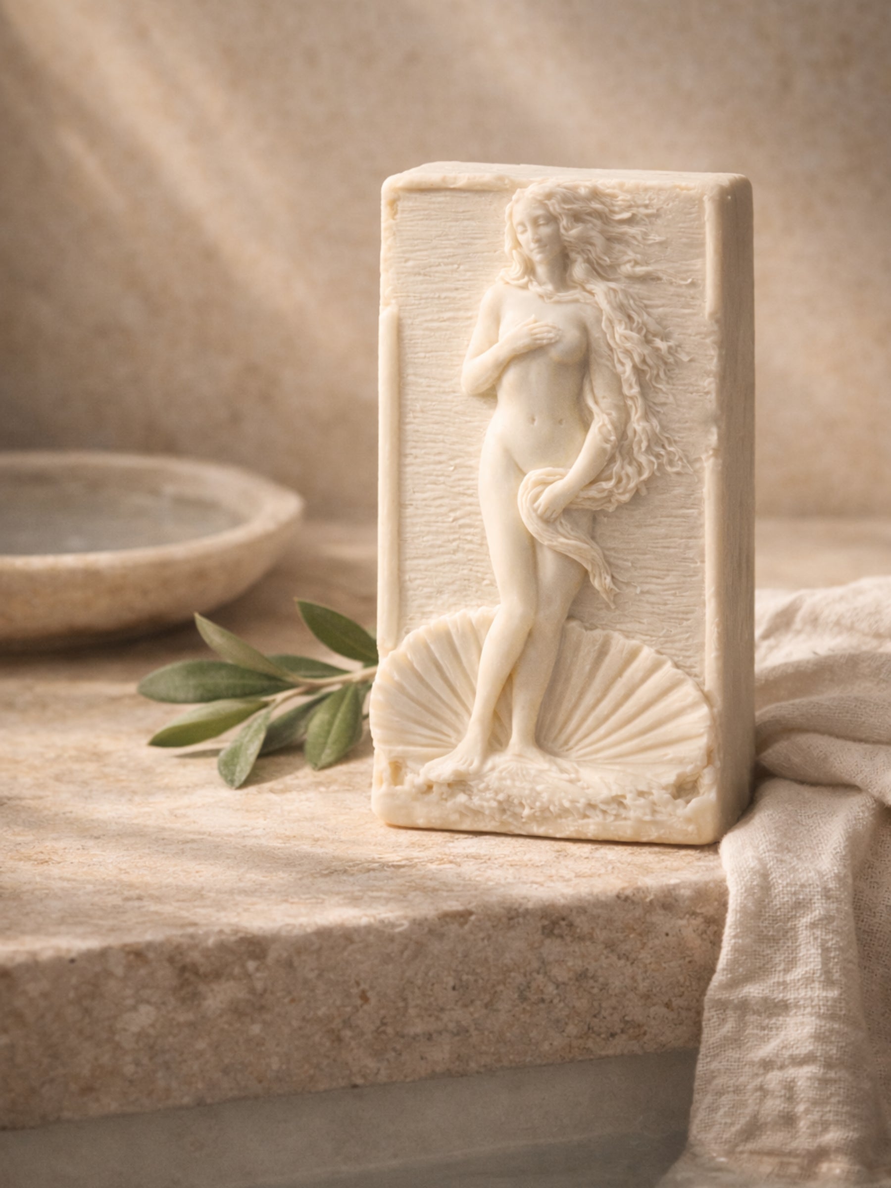 Sculptural olive oil soap with Aphrodite design displayed with green olives and lavender, natural luxury soap by DEOS Co.