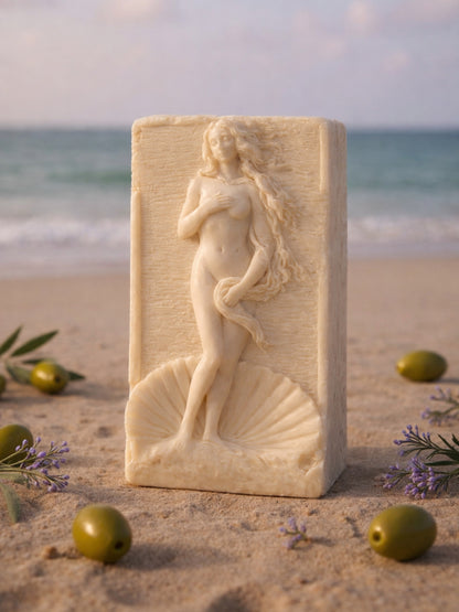 Handcrafted olive oil and lavender soap bar featuring Aphrodite Anadyomene relief, on a shell design on a sandy beach with olives and lavender by DEOS CO or DEOSCO