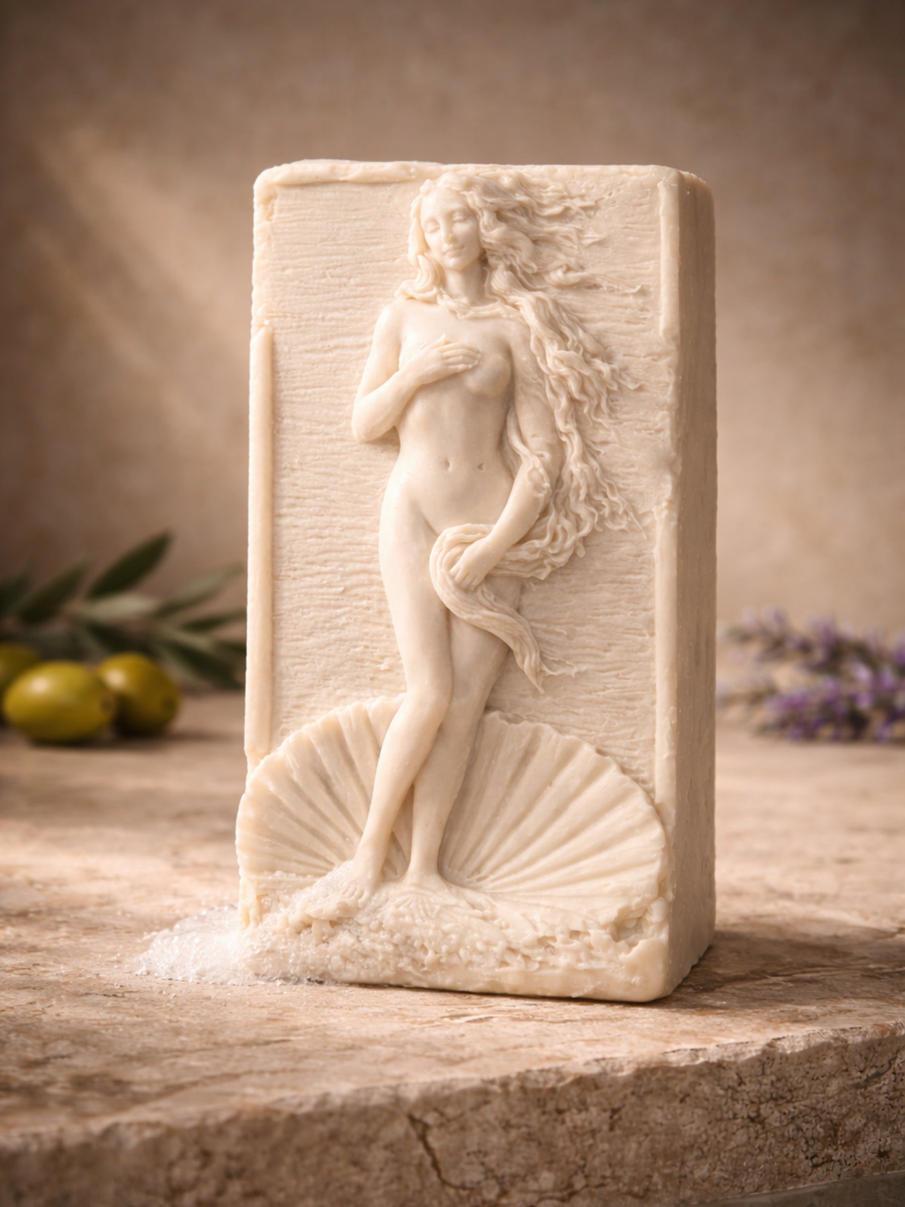 Sculptural olive oil soap with Aphrodite design displayed with green olives and lavender, natural luxury soap by DEOS Co.