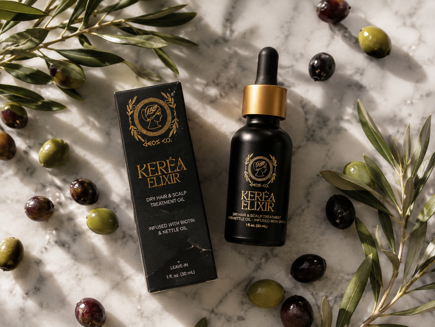 A bottle of Kereéa Elixir dry hair and scalp treatment oil with its black packaging box, styled on a white marble surface with olive branches and olives.
