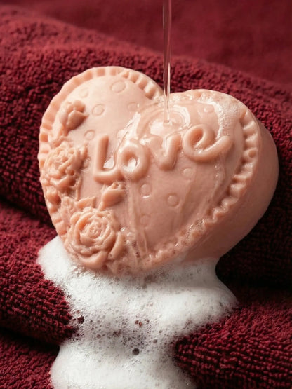 Heart-shaped soap with 'LOVE' and floral designs on a red towel by DEOS CO. Valentine Collection. Rose geranium and vanilla soap by DEOS CO