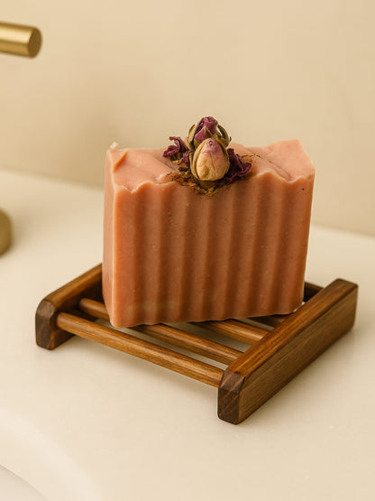 Bar of soap with dried flowers on Deos Co.'s natural wooden soap dish holder against a neutral bathroom background