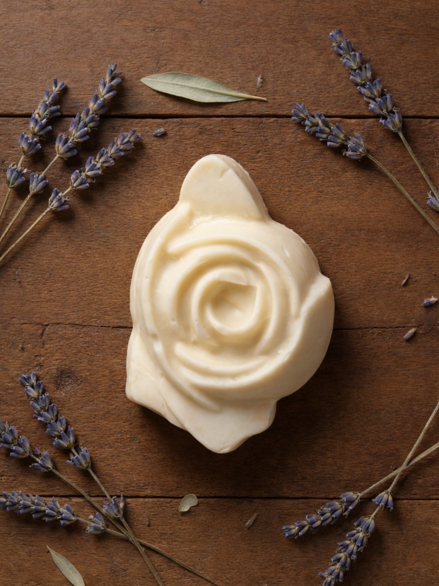 The Anthéa by DEOS CO., an ivory rose-shaped olive oil soap with dried lavender on a warm wooden surface
