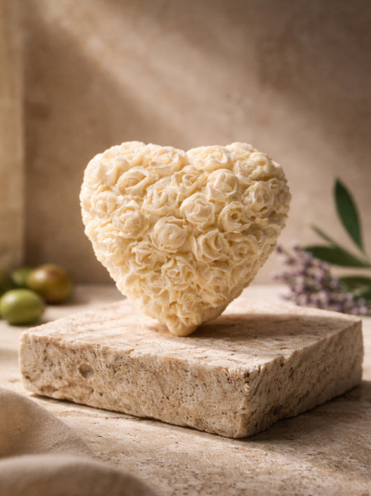 Small heart-shaped Fleur Heart soap intricately sculpted with floral details, standing upright on a natural stone pedestal with green olives and lavender stems in the background, Nardus Bliss Collection by DEOS Co.