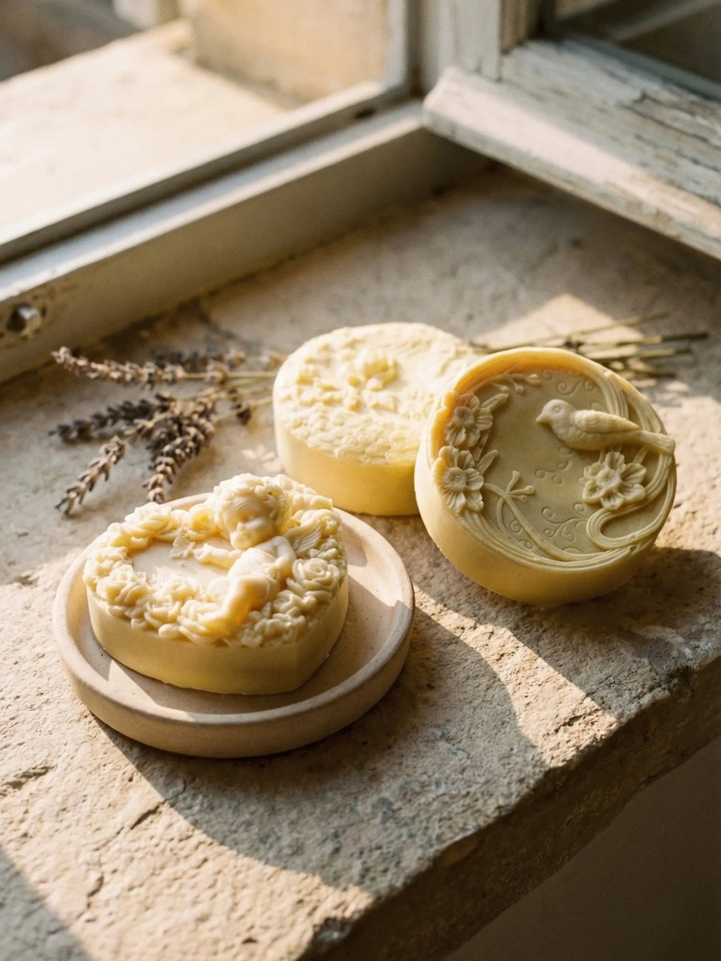 Artisan Greek olive oil lavender soaps from the Nardus Bliss collection arranged beside fresh olive leaves and linen cloth. The herald soap, the hera peacock soap, the eros angel olive oil soap by DEOS CO.