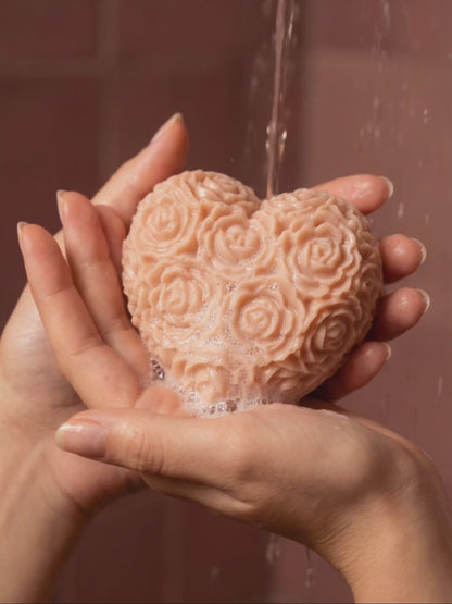 Heart-shaped The Fleur Grand Bloom rose-patterned rose geranium vanilla soap being held with water dripping from it against a brown background by DEOS CO