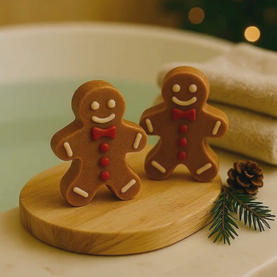 Pair of Deos Co. Golden Gingerbread Glow soaps beside a warm bath, natural Christmas spa setting with festive pine decor and cozy lighting.
