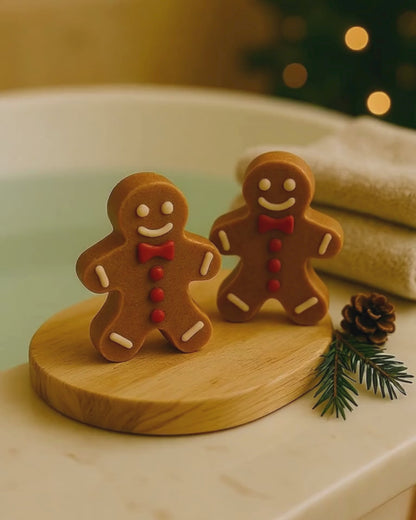 Pair of Deos Co. Golden Gingerbread Glow soaps beside a warm bath, natural Christmas spa setting with festive pine decor and cozy lighting.
